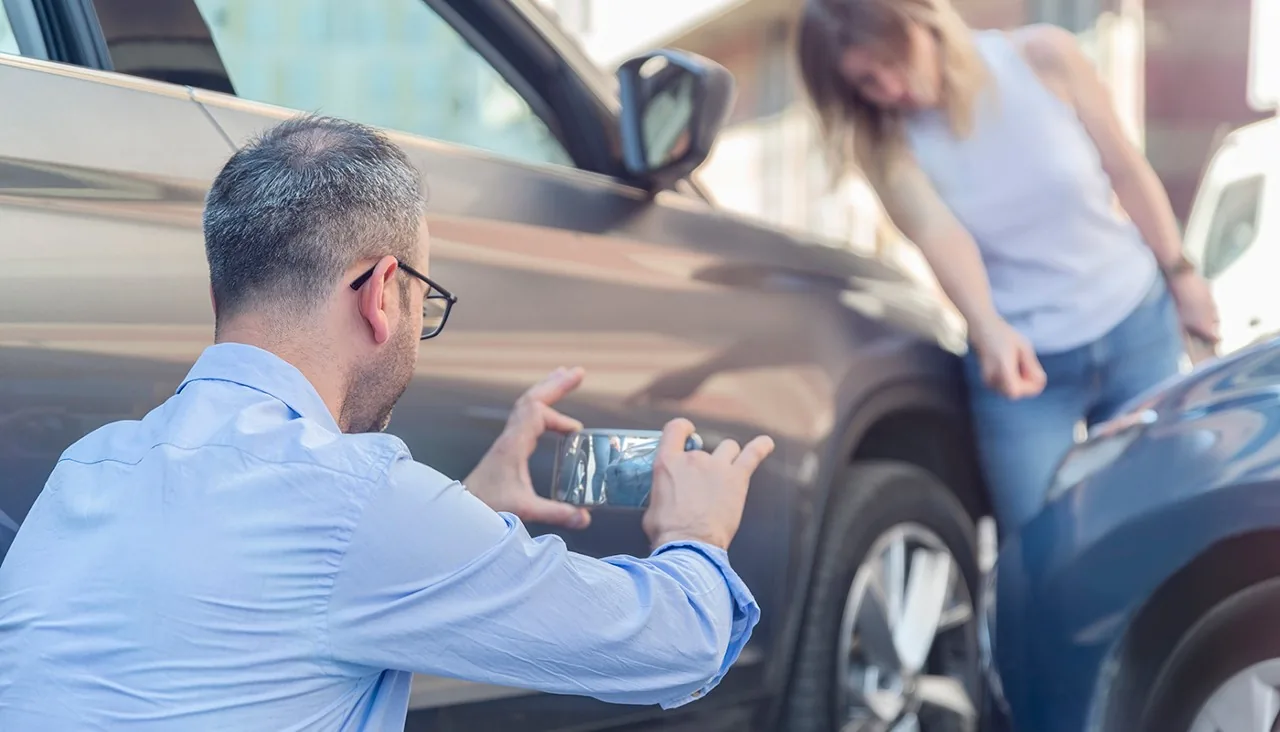 An adjuster photographing damage to a car while the driver looks on