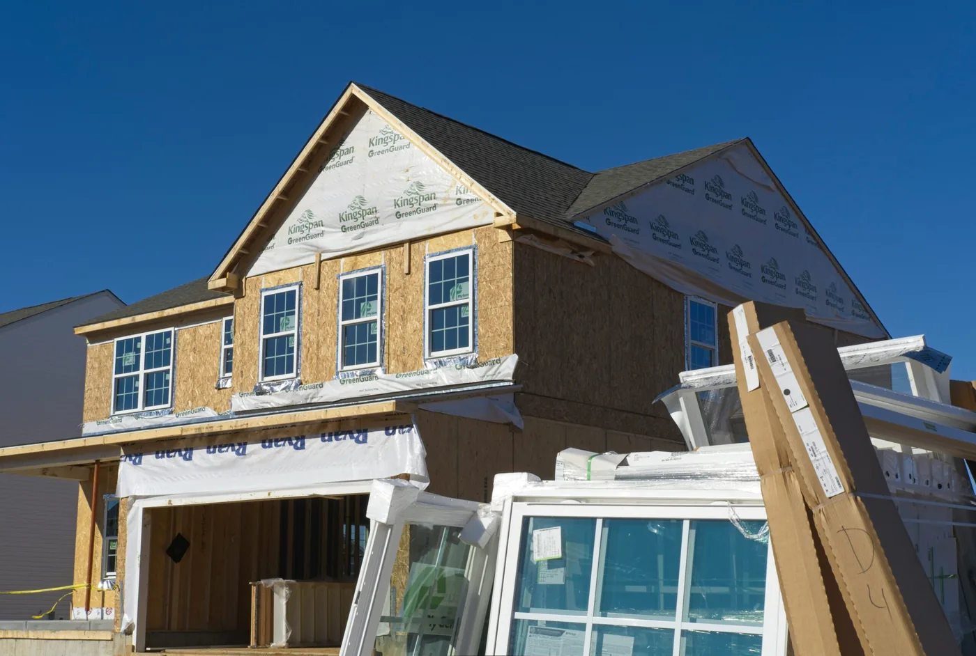 A house under construction with new windows stacked against the frame